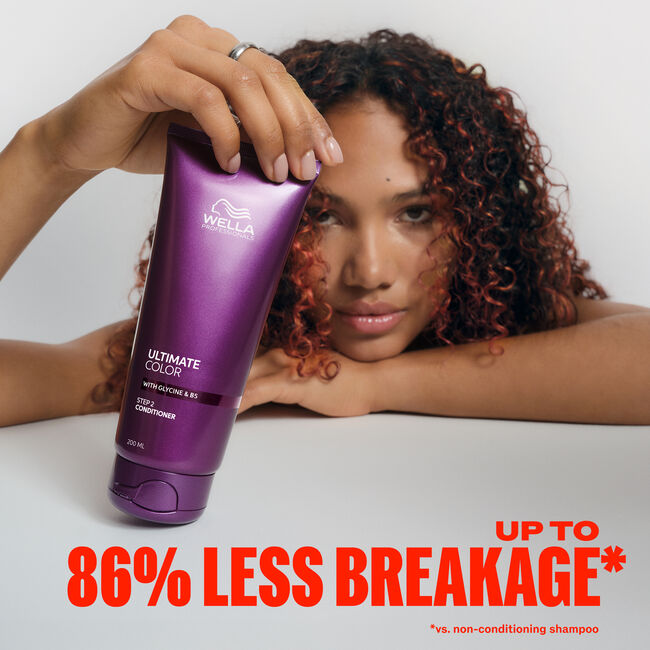 Wella Ultimate Color Conditioner tube held by a model with red curls - up to 86% less breakage versus non-conditioning shampoo