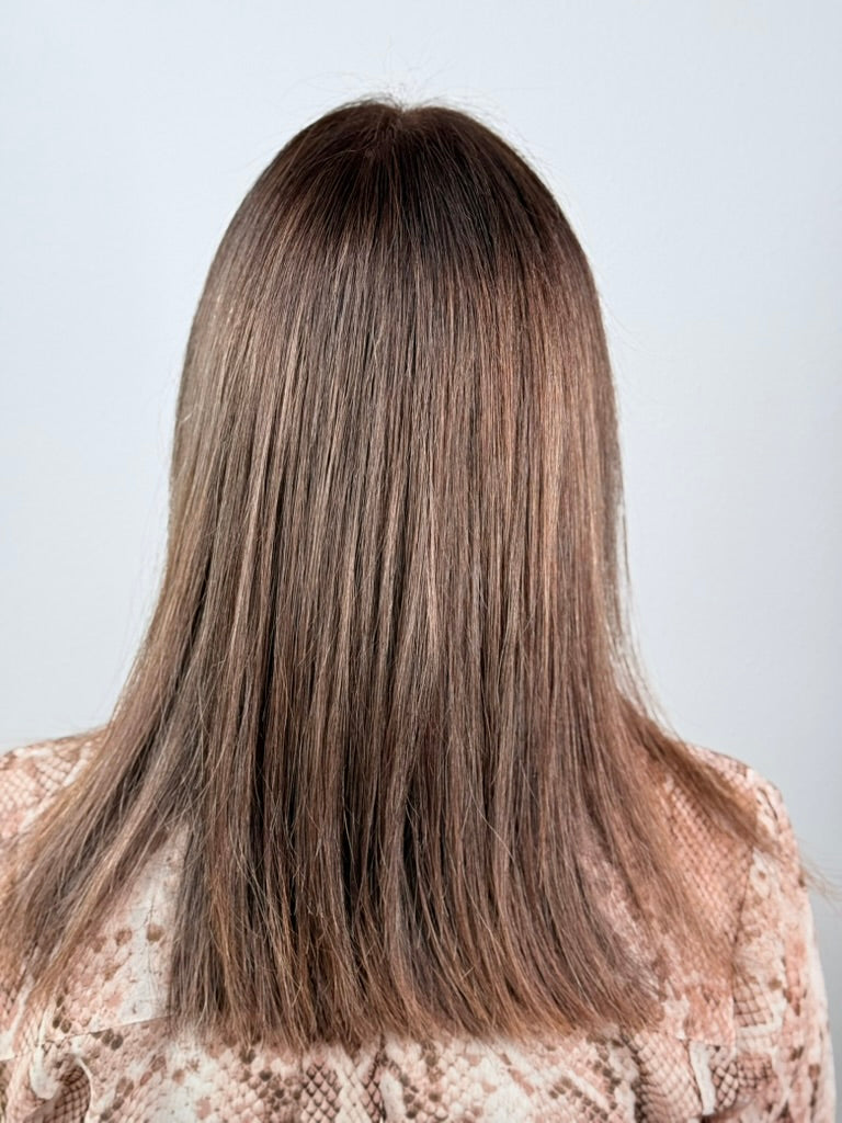 Person with long, straight brown hair wearing a patterned top on a light gray background