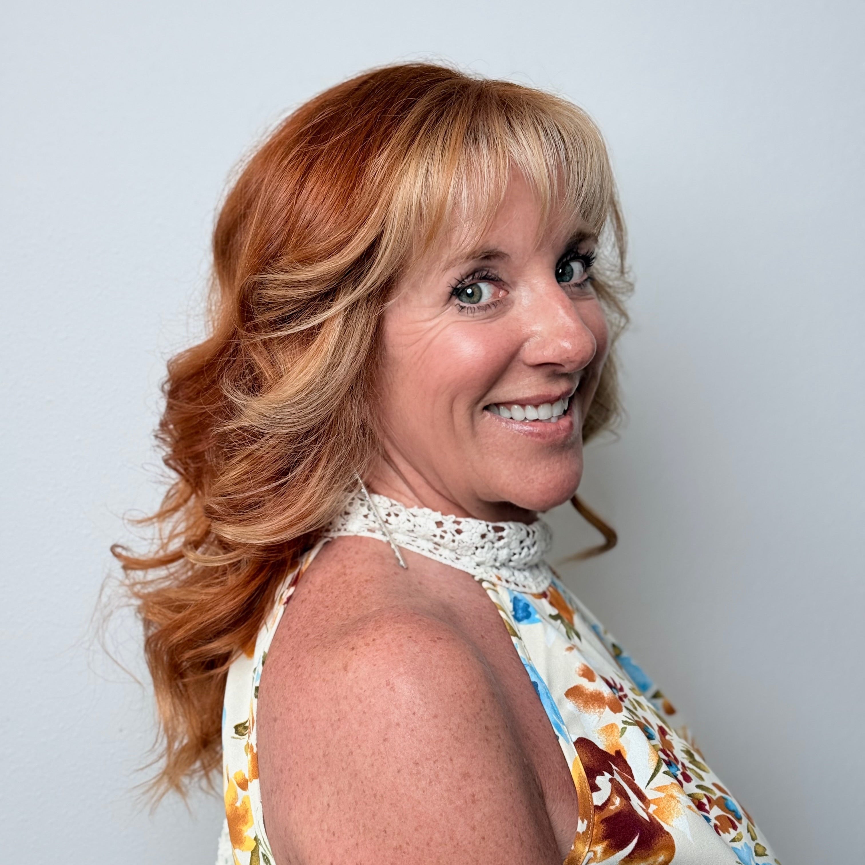 Woman with shoulder-length blonde hair wearing a floral dress against a light gray background