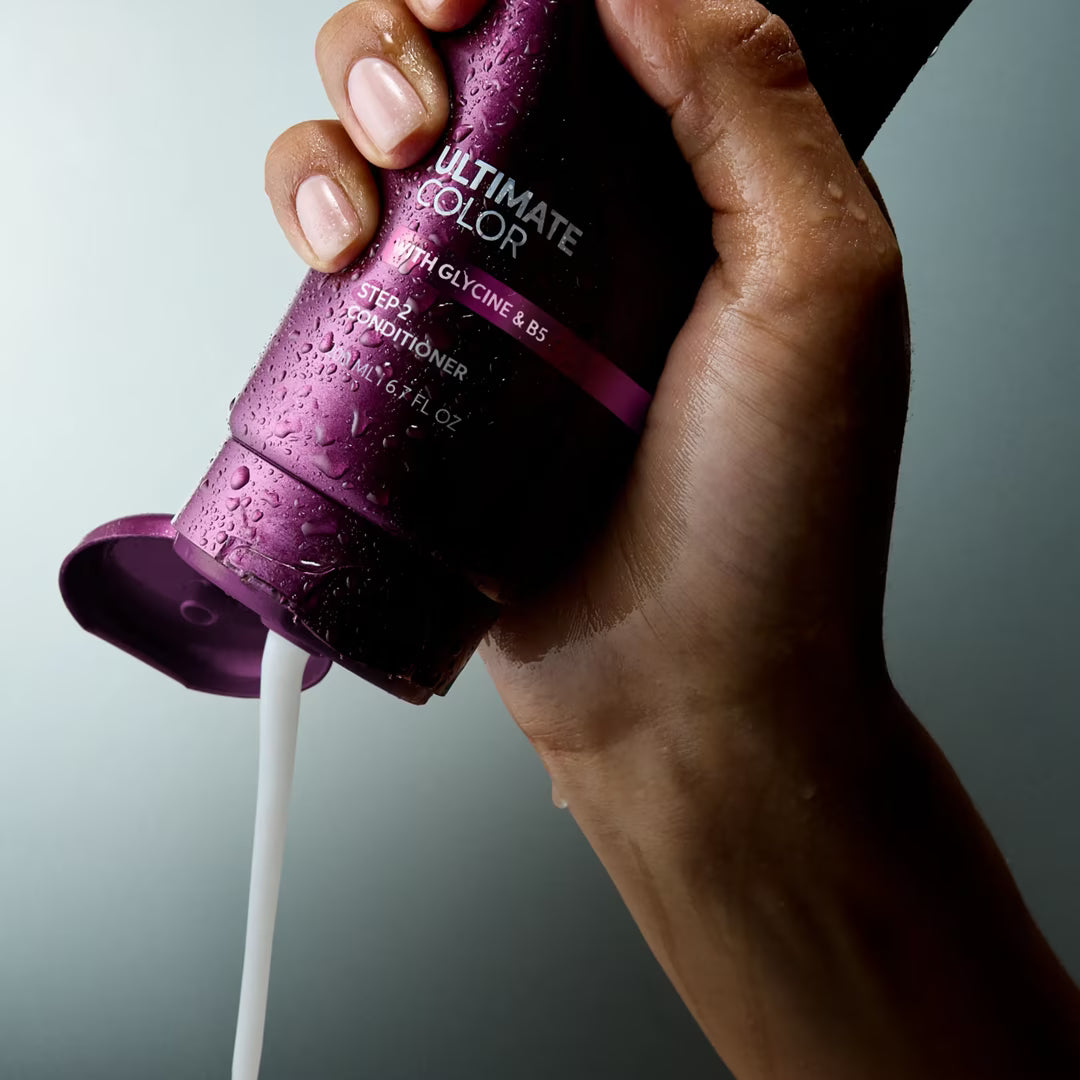 Hand holding a purple bottle of 'Ultimate Color' conditioner with white liquid being poured.