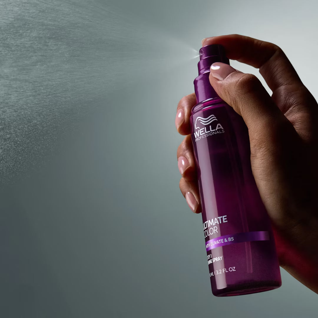 Hand holding a purple Wella spray bottle against a gray background