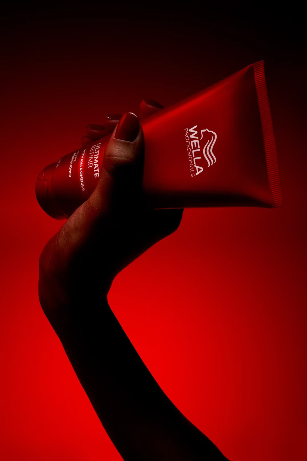 Hand holding a Wella hair care product against a red background