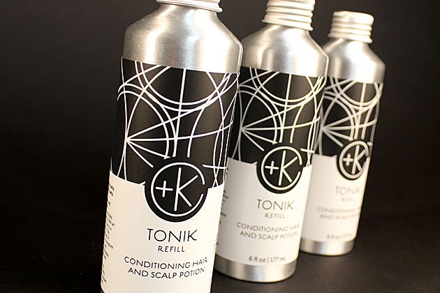 Three silver Cult and King TONIK Conditioning Hair & Scalp Potion bottles with black and white geometric labels are shown: two stand upright (hair conditioner), while one (scalp tonic) sits behind them with the cap off.