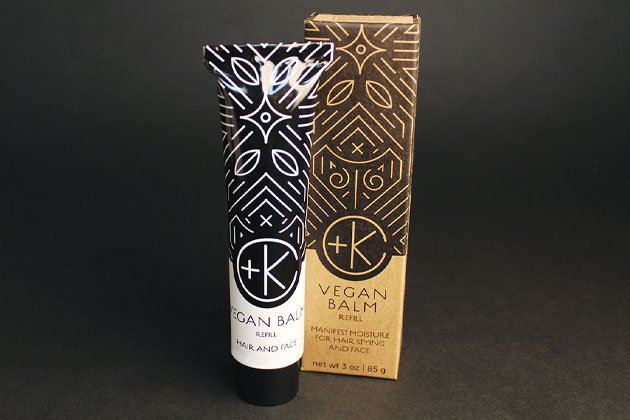 A black-and-white tube labeled “Cult and King VEGAN BALM | Manifest Moisture for Hair Styling and Face” stands by its matching geometric-patterned box; this refill styling balm contains botanical oils for hair and face.