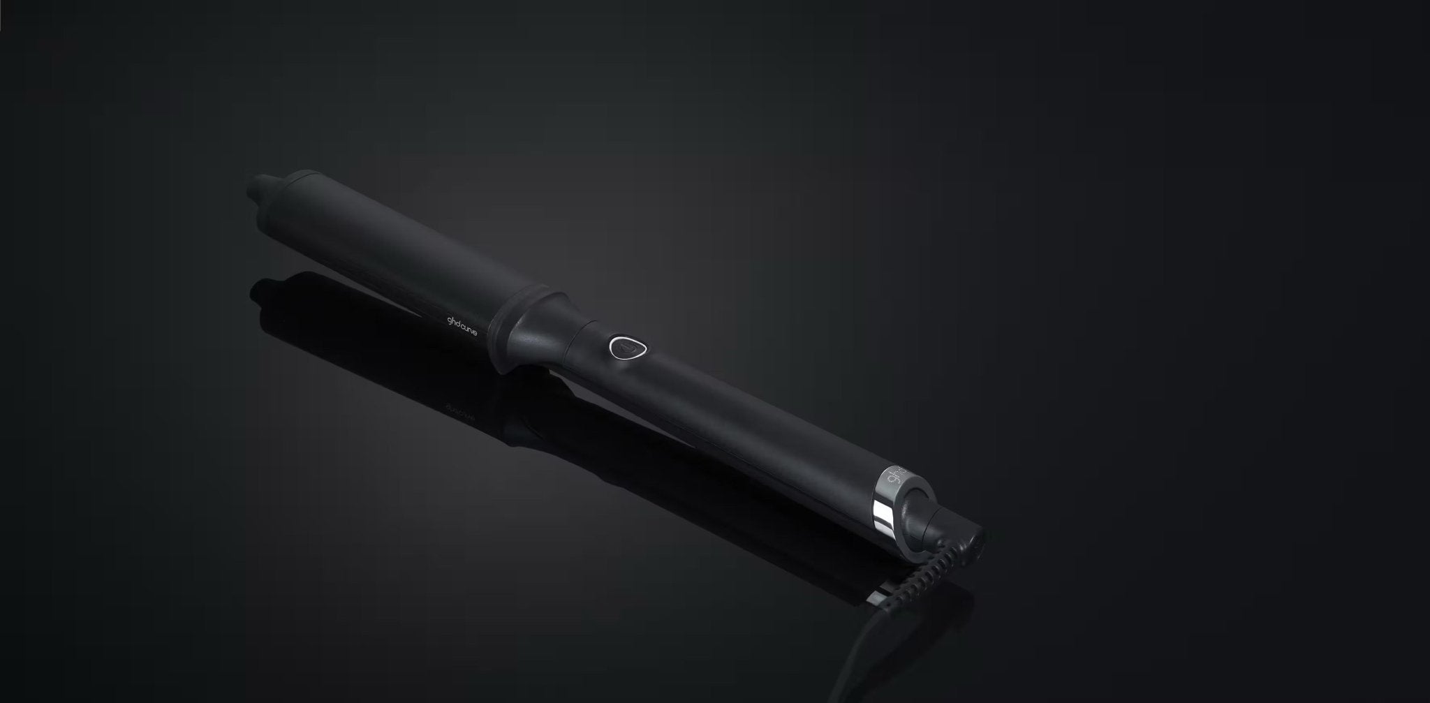 The GHD CLASSIC WAVE - OVAL CURLING WAND by GHD features a ceramic-coated barrel and power button, ideal for creating Hollywood waves, shown here on a dark reflective surface.