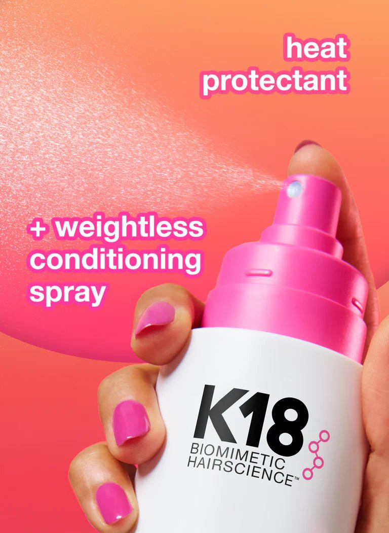 K18 hair care product with pink spray nozzle held by a hand against a gradient background