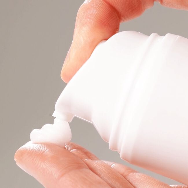 Hand applying a small amount of white cream to another hand against a neutral background