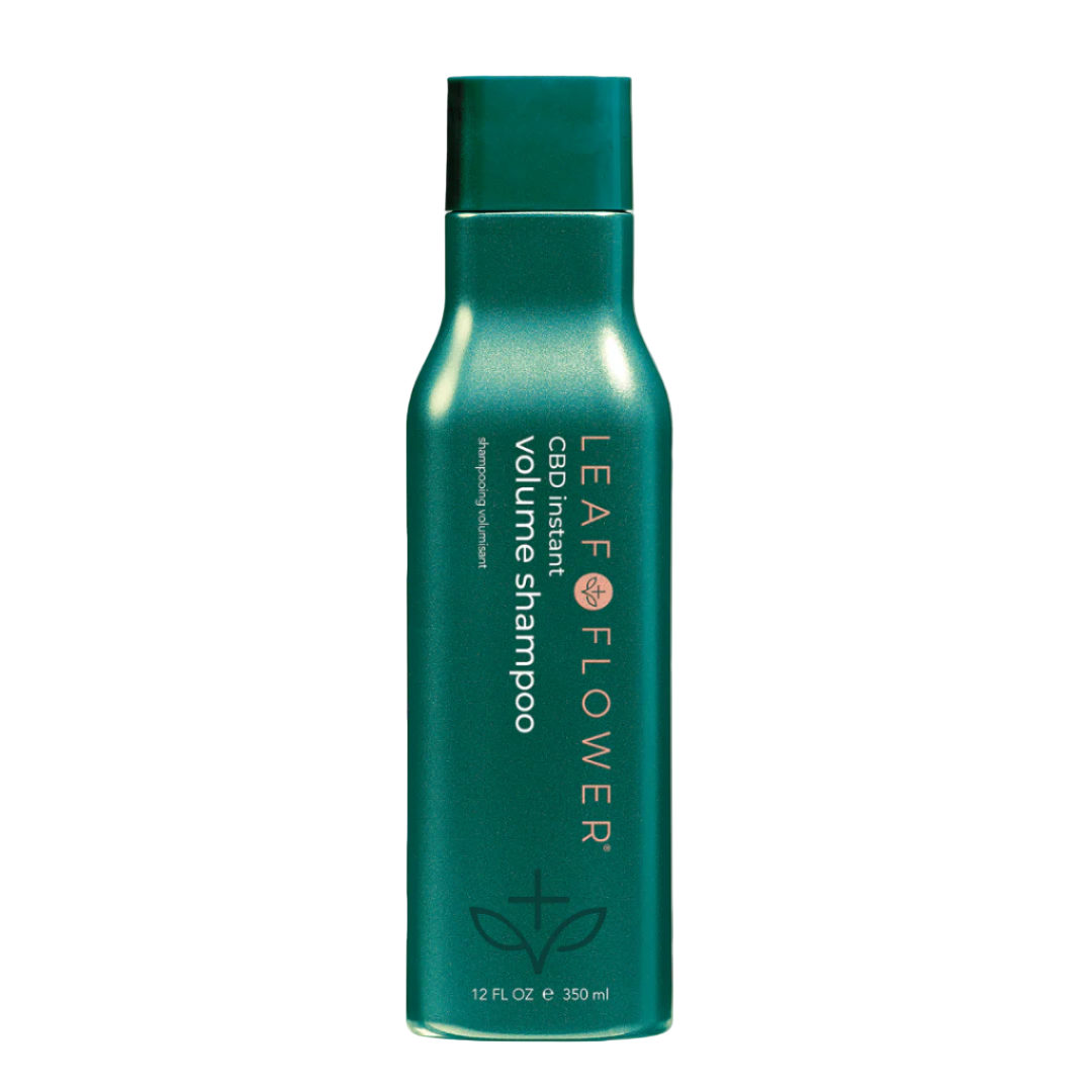 A green bottle of Leaf and Flower Instant Volume Shampoo (multiple sizes available) stands upright, showing its sulfate-free, plant-based formula with the product name and logo in white and gold text on a light background.