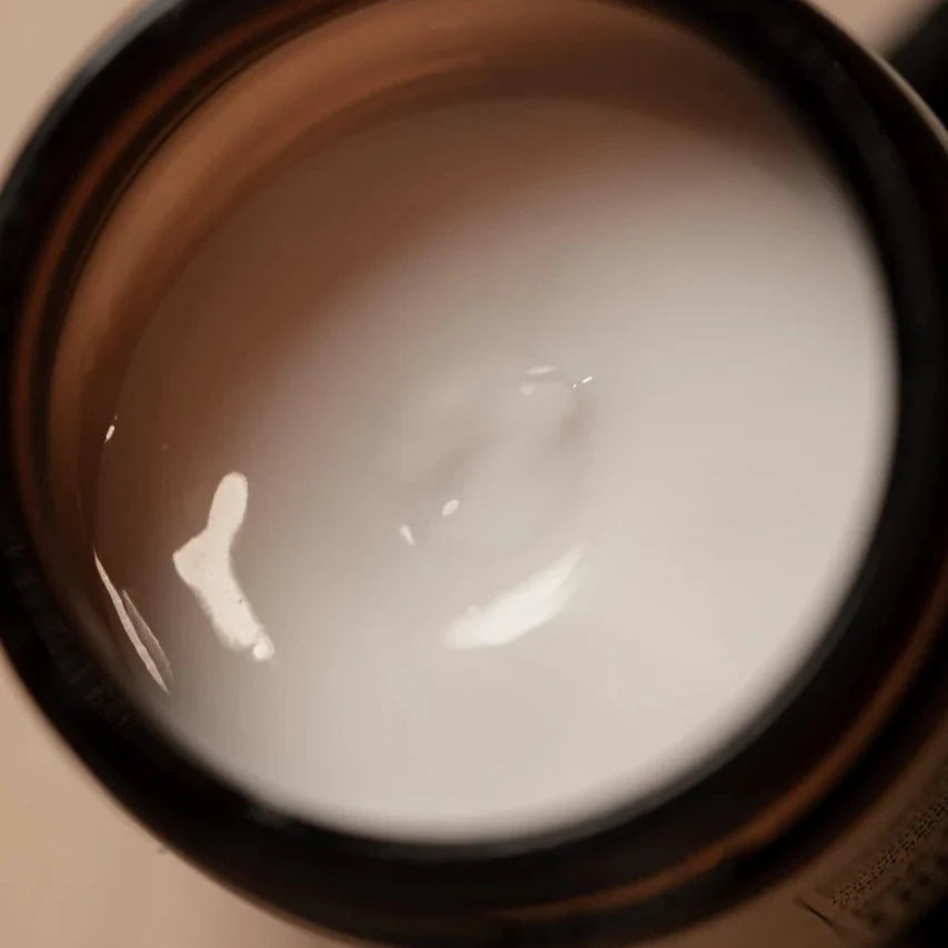A close-up of an open jar of Oway Boho Pomade, a creamy white texturizing cream pomade for a laid-back, matte finish, with a smooth surface and subtle light reflection.