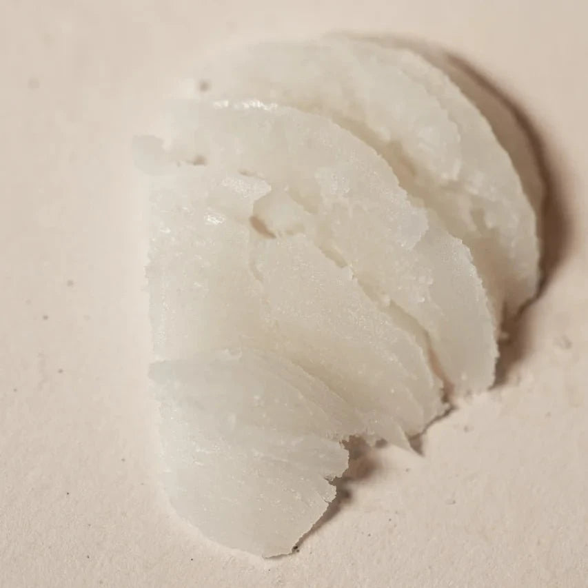A close-up of Oway Precious Wax by Oway, featuring several oval slices with a translucent white, slightly waxy texture and luminous shine, arranged on a plain surface to showcase its natural definition and shine-enhancing qualities.