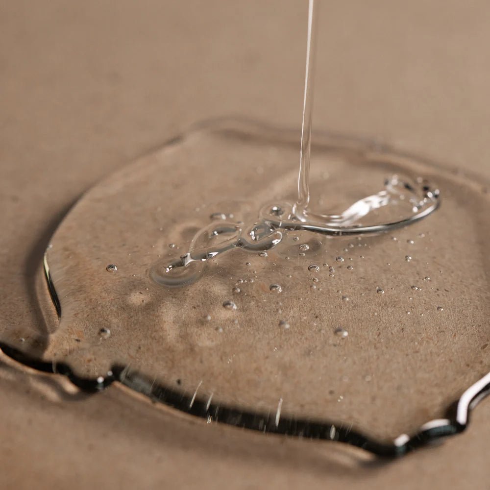 A close-up shows Oway Purifying Hair Bath for Oily Scalp, a transparent liquid forming bubbles on a beige surface—ideal for highlighting this organic Oway shampoo that effectively prevents dandruff and cares for oily scalps.