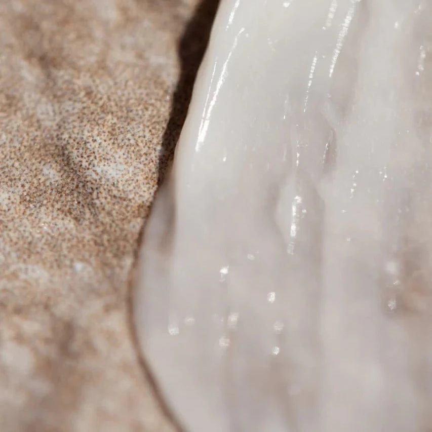 A close-up view of Oway Rebuilding Hair Mask, a white creamy restorative mask for damage and instant repair, spread on a textured brown surface—highlighting its rich texture, ideal for treating chemically treated hair.