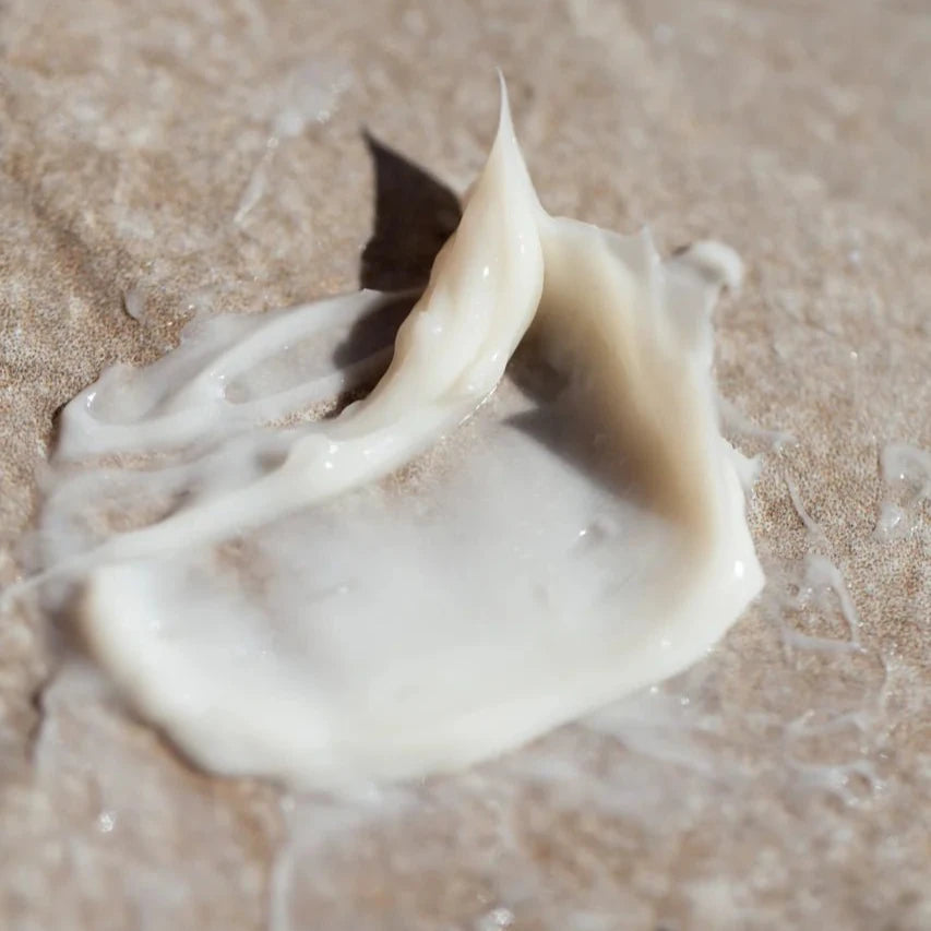 A close-up of a small smear of Oway Silk’N Glow Hair Mask—a nourishing mask for dry, frizzy hair—on a textured beige surface.