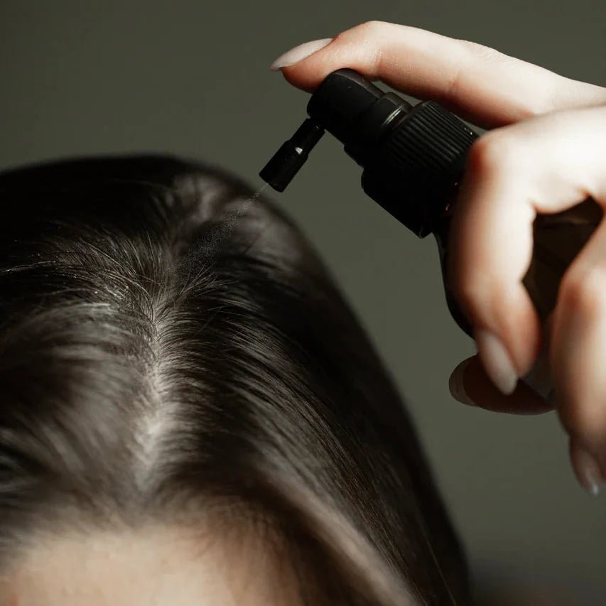 Hand holding a black spray bottle over a person's head against a dark background