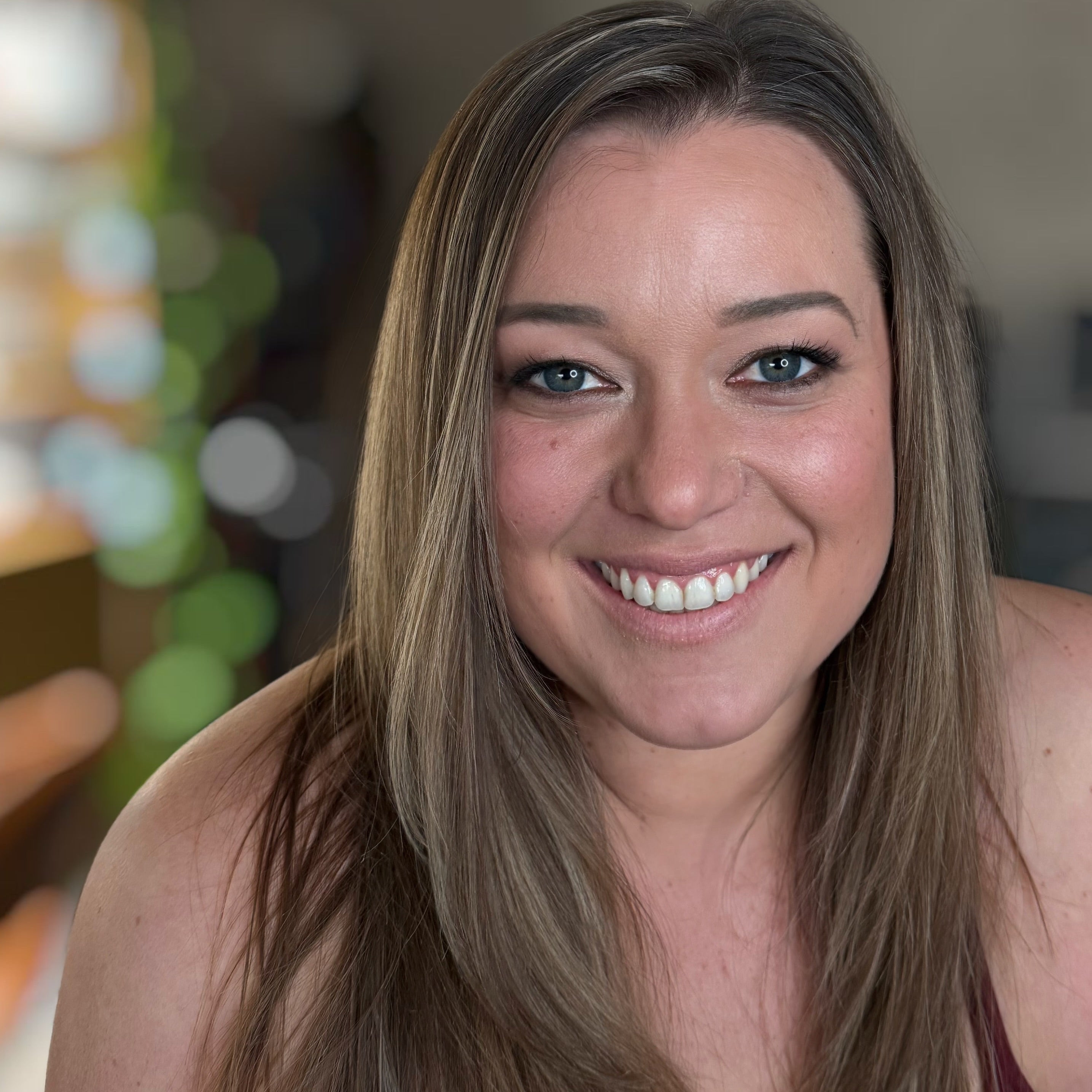 Woman with long brown hair smiling at the camera with a blurred background