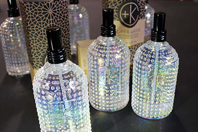 Three iridescent, studded glass bottles with black caps display Cult and King SUPER WATER, an antioxidant toner for hair and skin. Elegant packaging in the background evokes vegan luxury by Cult and King.