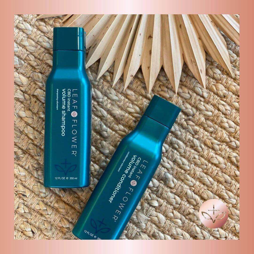 Two teal bottles of Leaf and Flower Instant Volume Shampoo and Conditioner Duo for fine hair rest on a woven surface with a dried palm leaf in the background, highlighting their vegan-friendly volumizing formula.