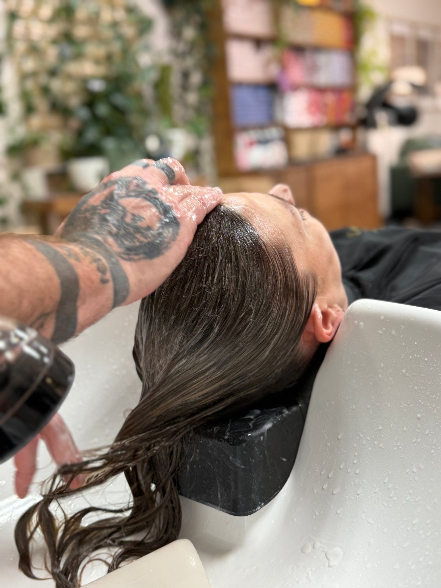 a woman recieving a shampoo with plants and shelves in the background