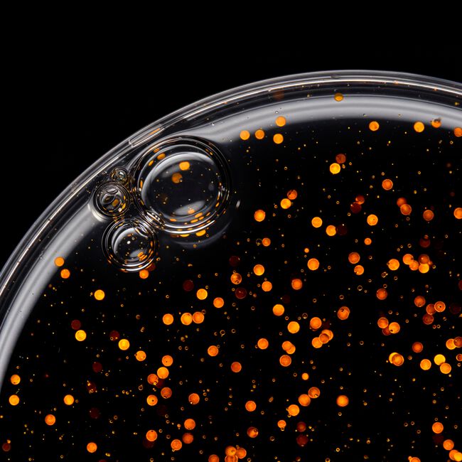 Close-up of a dark liquid with orange and red specks on a black background