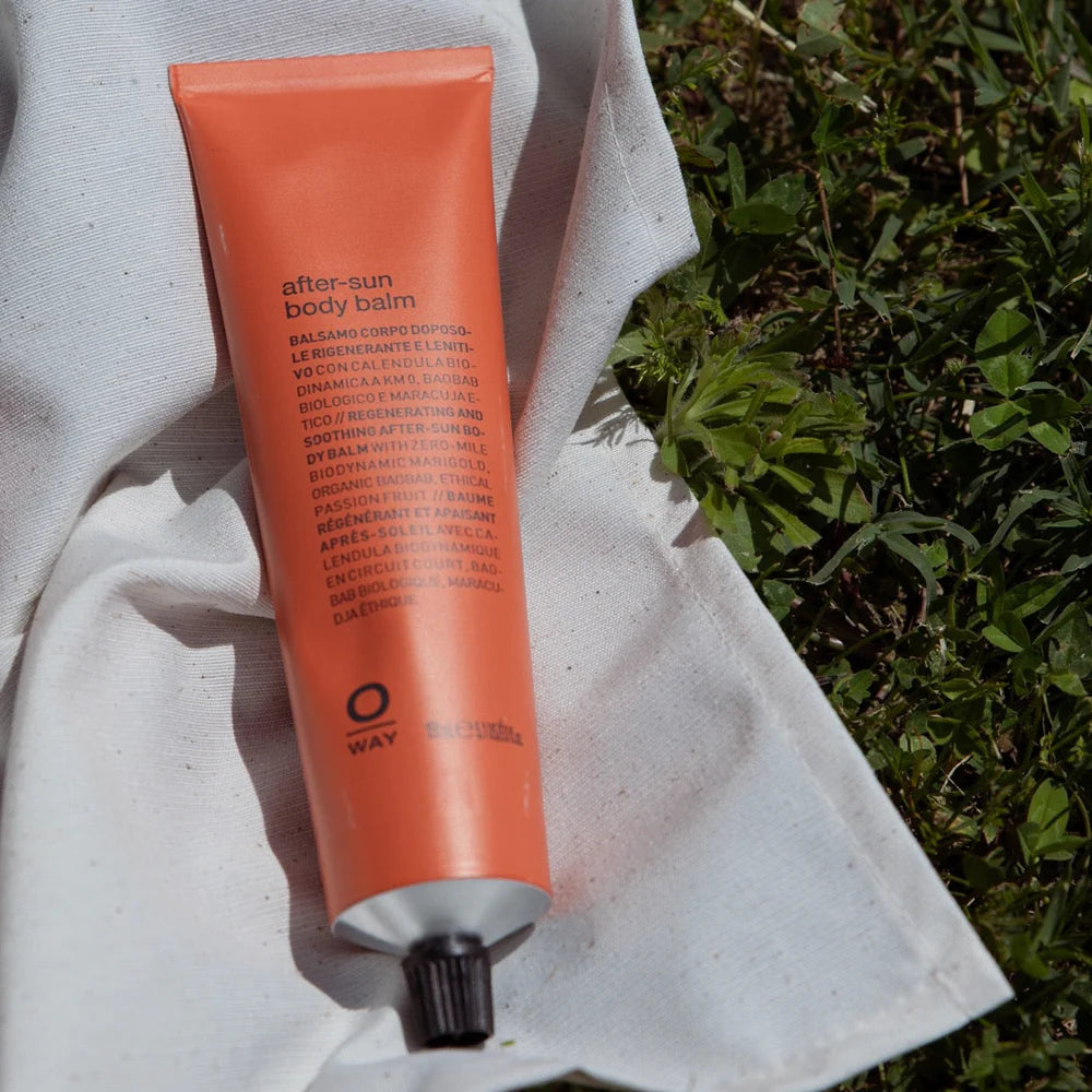 An orange tube of Oway After Sun Body Balm sits on a white cloth by green grass, showcasing this nourishing organic balm that soothes and hydrates sun-exposed skin with biodynamic botanicals.
