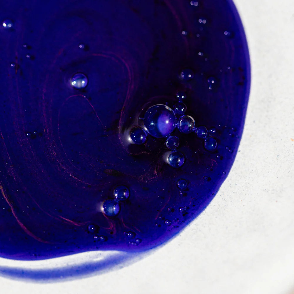 Close-up of Oway Bluemoon Hair Bath, an illuminating anti-yellow shampoo for cool blonde, white & grey hair, with bubbles on a white surface, formulated to neutralize brassiness.