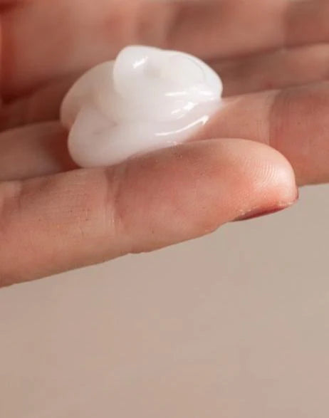 A close-up of fingers holding a dollop of Oway Frequent Use Conditioner, a lightweight formula for everyday use, against a neutral background.