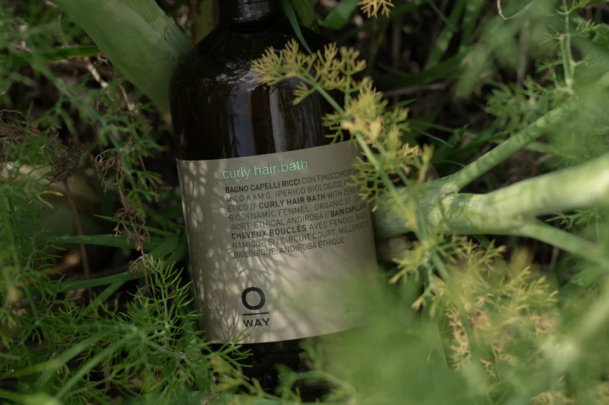 An Oway Curly Hair Bath bottle—sulfate-free cleanser for wavy and curly hair—sits among lush outdoor greenery.