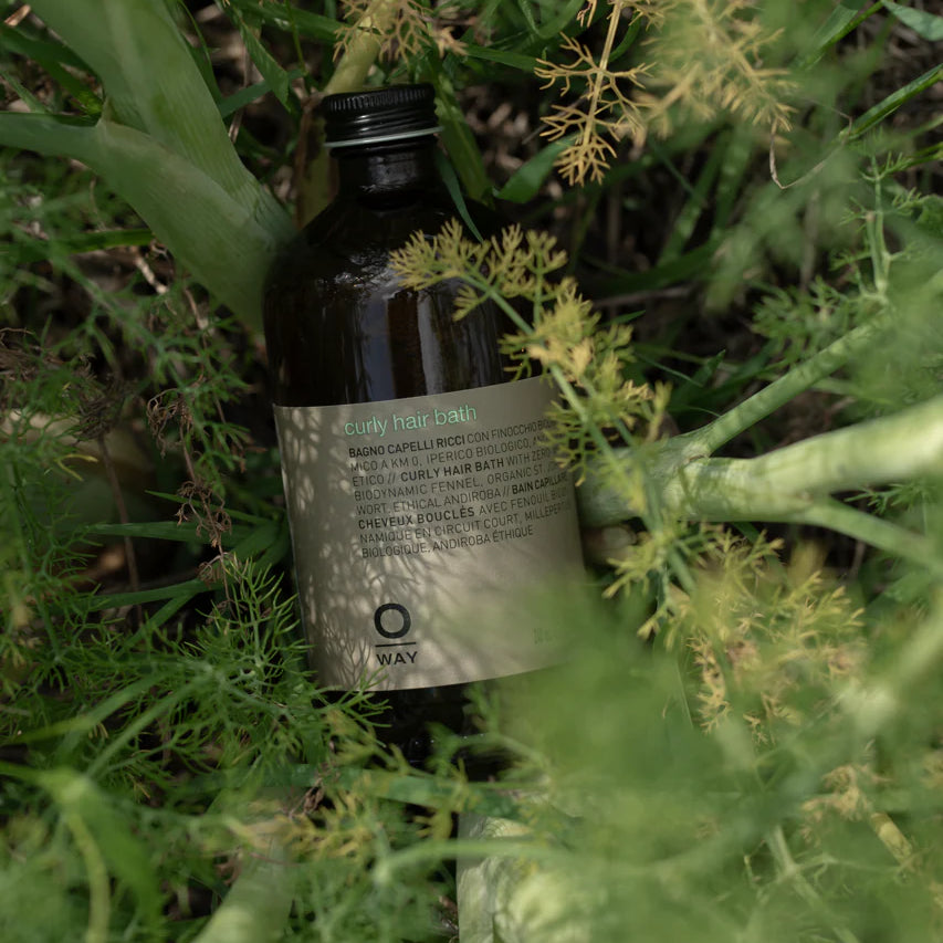An Oway Curly Hair Bath bottle—sulfate-free cleanser for wavy and curly hair—sits among lush outdoor greenery.