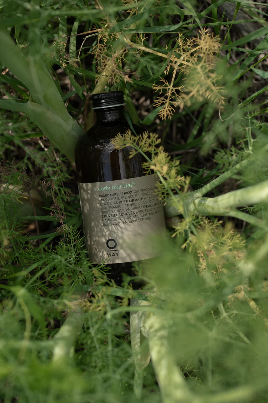 An Oway Curly Hair Bath bottle—sulfate-free cleanser for wavy and curly hair—sits among lush outdoor greenery.