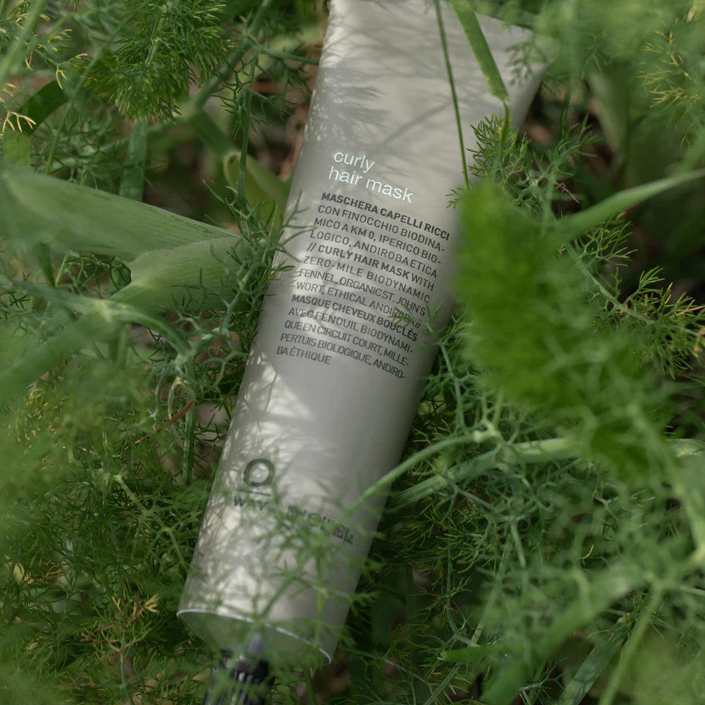 A tube of Oway Curly Hair Mask | Definition and Moisture Mask for Natural Curls rests among green leaves, its front label showing product details in multiple languages.