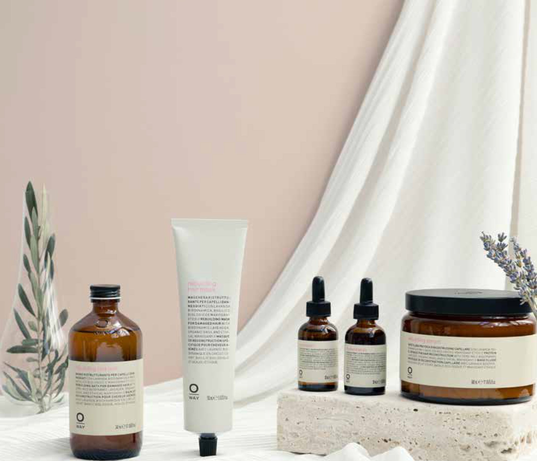 The Oway Rebuilding Hair Mask, a restorative mask for damage and instant repair, in amber packaging is displayed on light fabric with small plants and a textured stone.