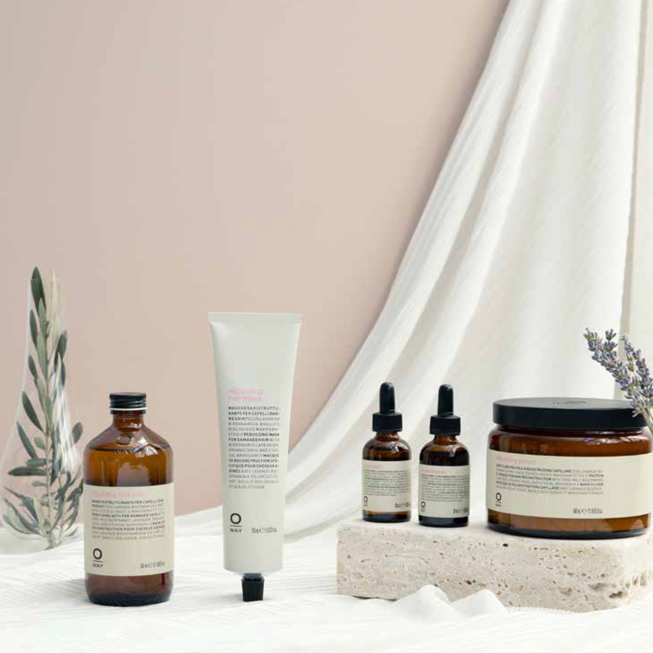 The Oway Rebuilding Hair Mask, a restorative mask for damage and instant repair, in amber packaging is displayed on light fabric with small plants and a textured stone.