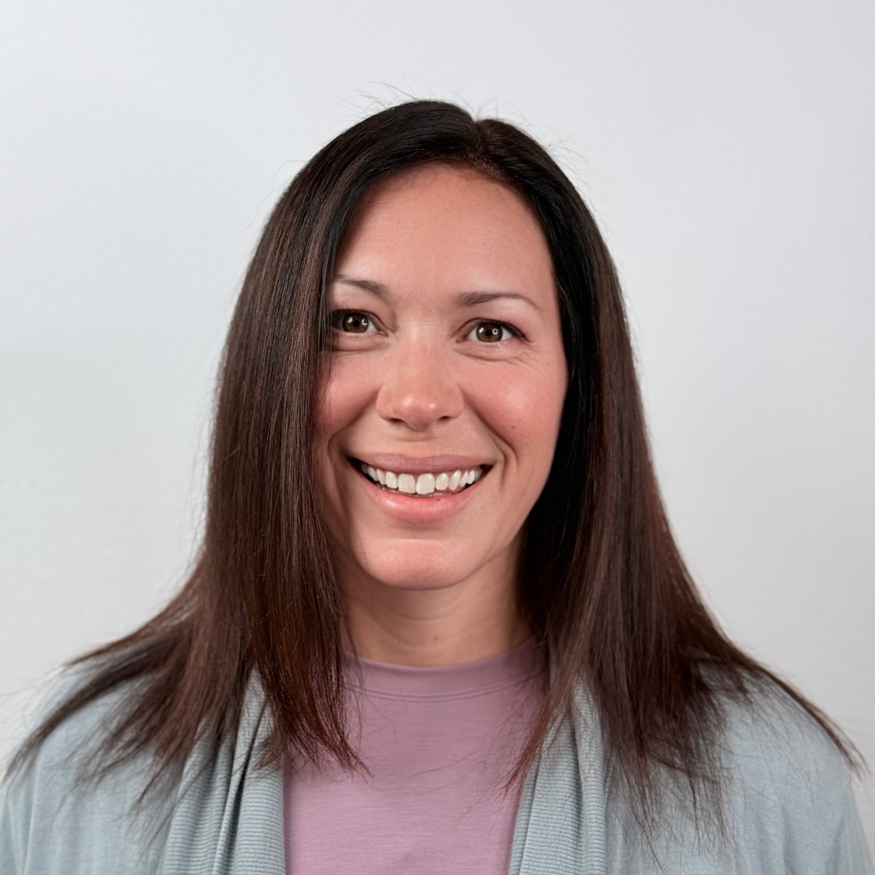 Woman with long dark hair wearing a light blue cardigan over a purple shirt against a white background