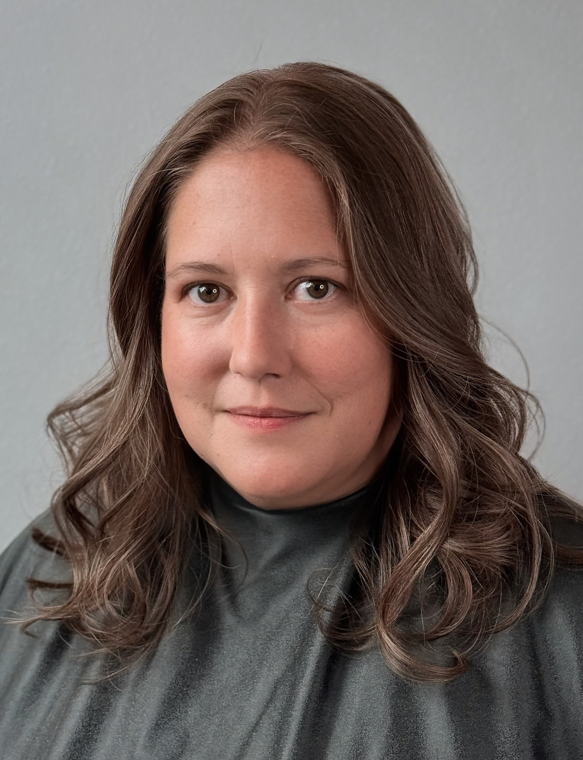 Woman with wavy brown hair wearing a gray sweater against a plain background