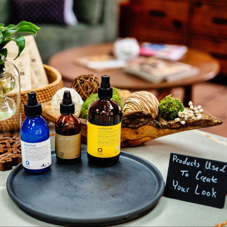 Three bottles of hair care products on a tray with decorative items in the background