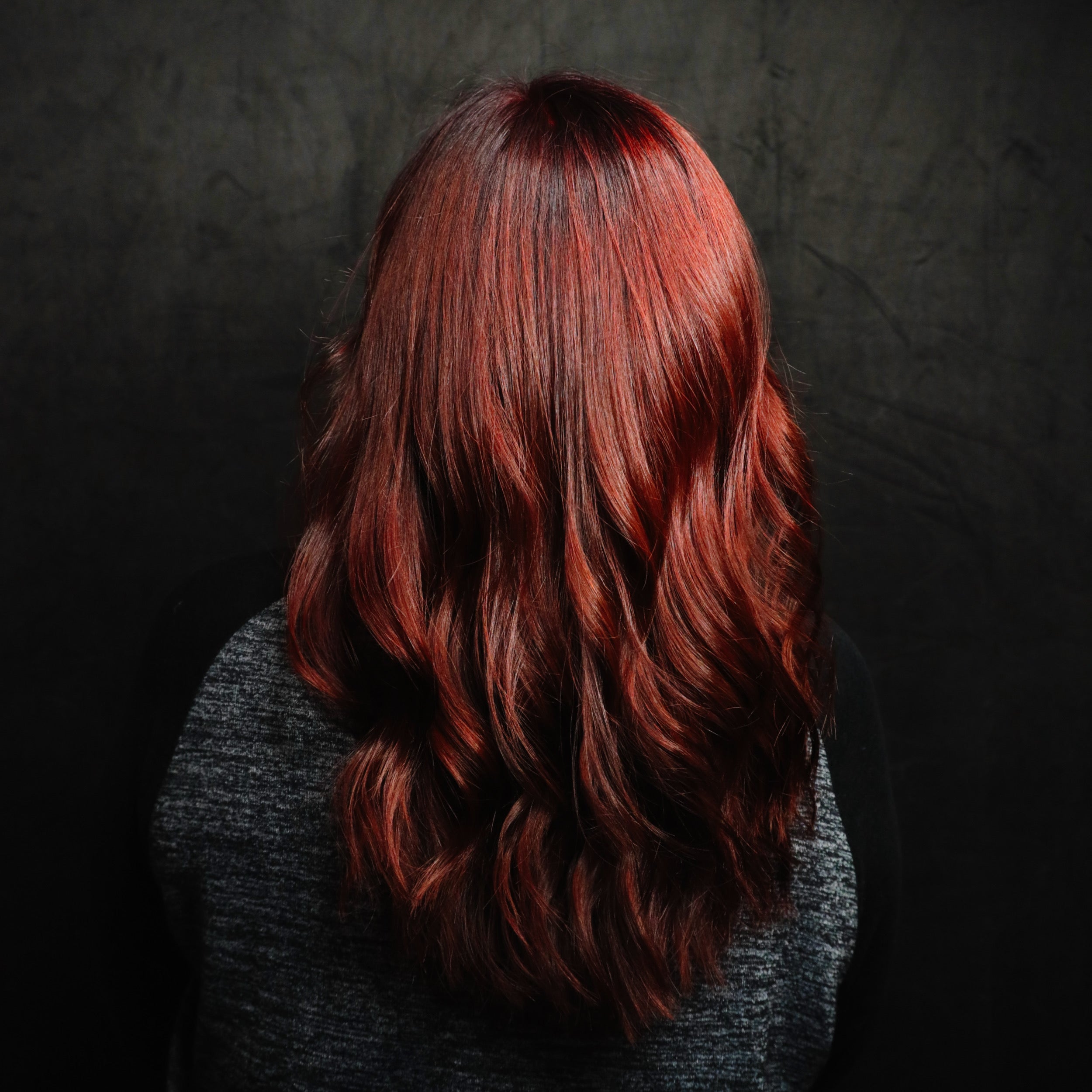 Person with long, wavy red hair against a dark background
