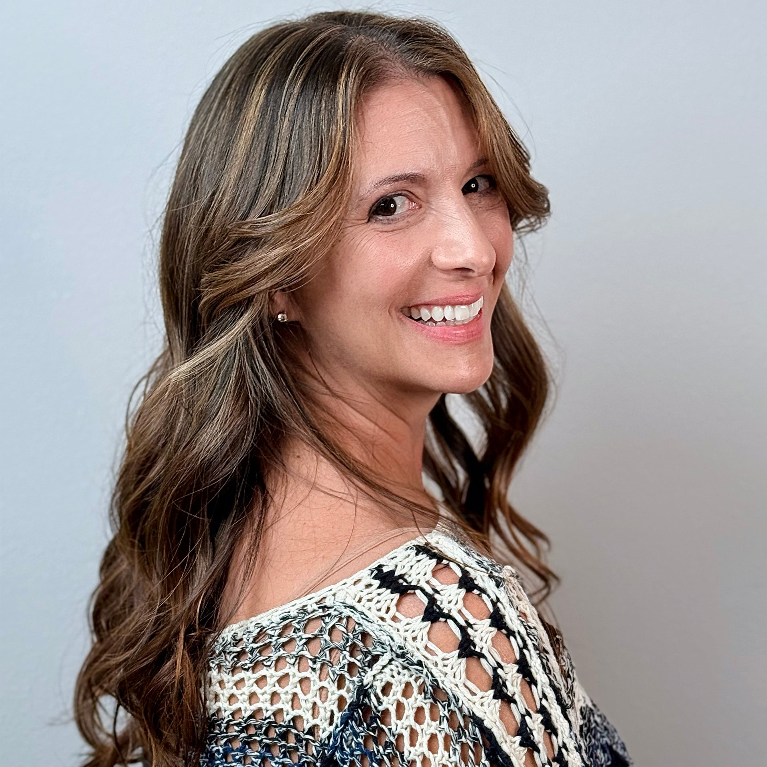 Woman with long brown hair wearing a patterned top against a plain background