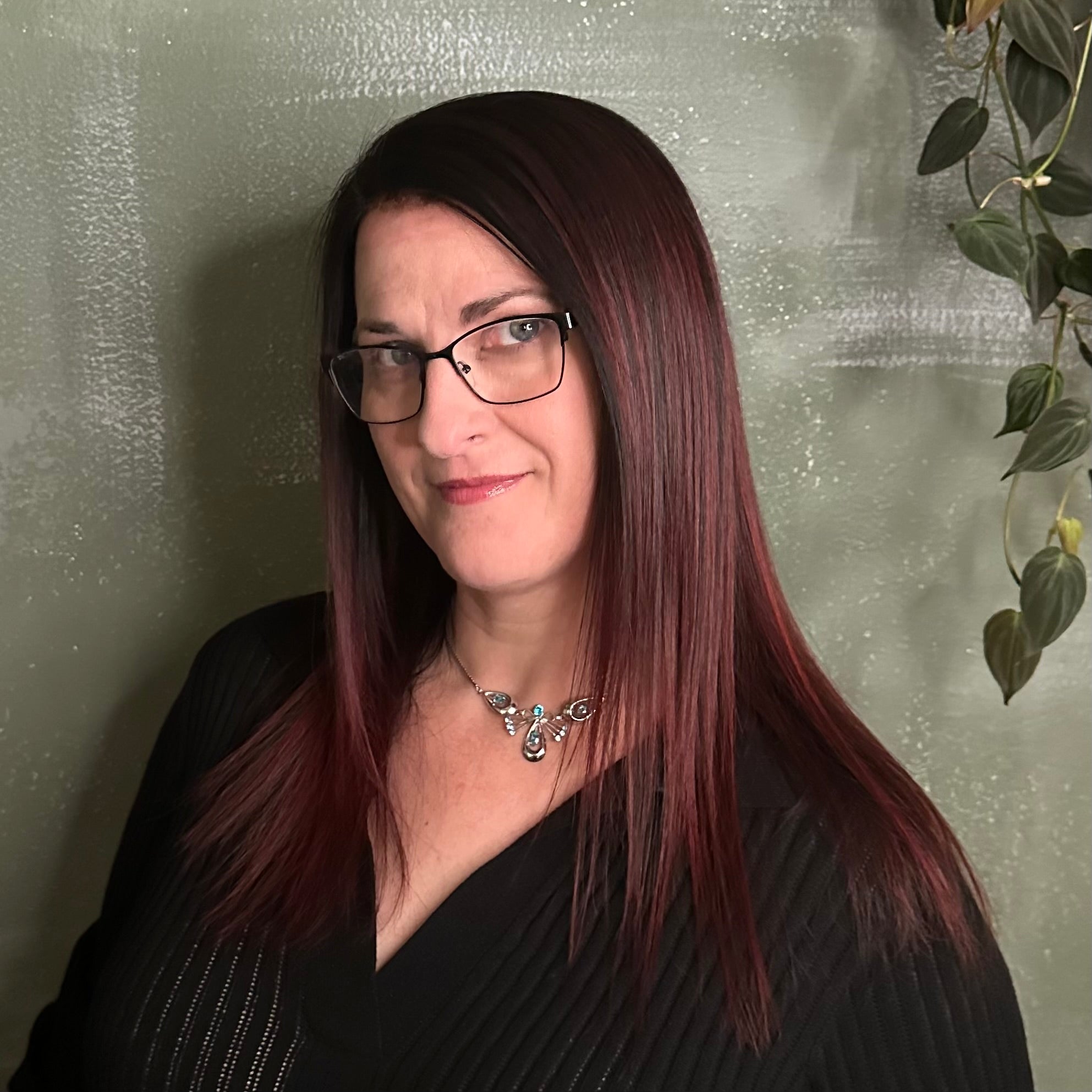 Woman with glasses and a black top against a textured wall.