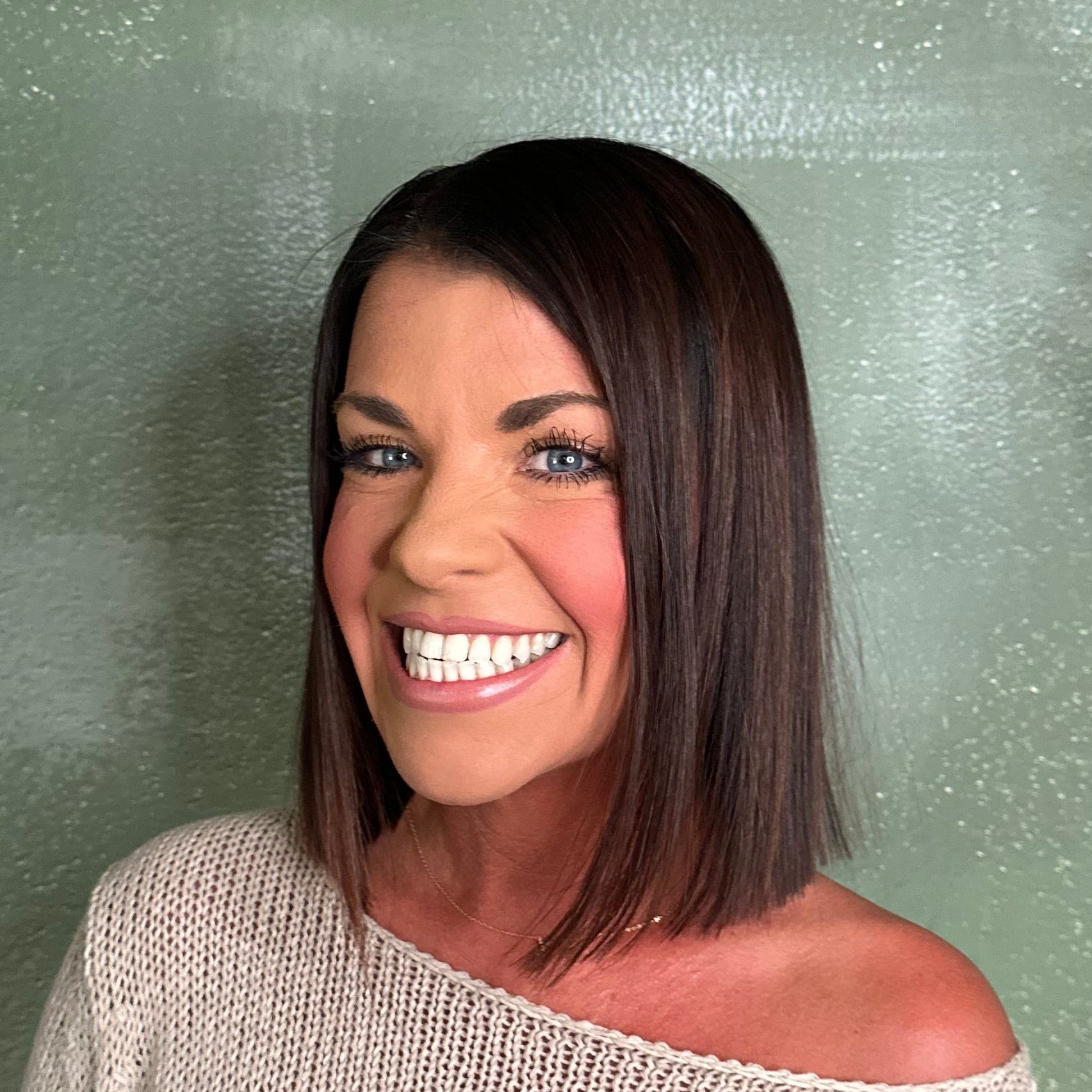 Woman wearing a 'Lake Life' sweater standing against a light green wall with plants.