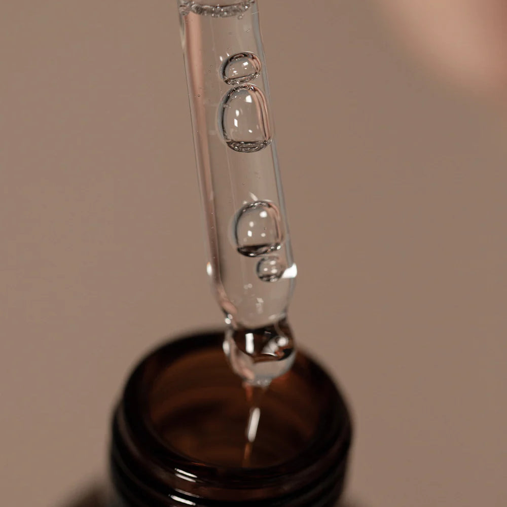 A close-up of Oway Nurturing Drops, a silkening serum for split ends and heat protection, in a dropper above the dark glass bottle.