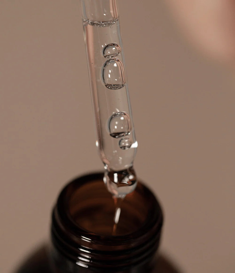 A close-up of Oway Nurturing Drops, a silkening serum for split ends and heat protection, in a dropper above the dark glass bottle.