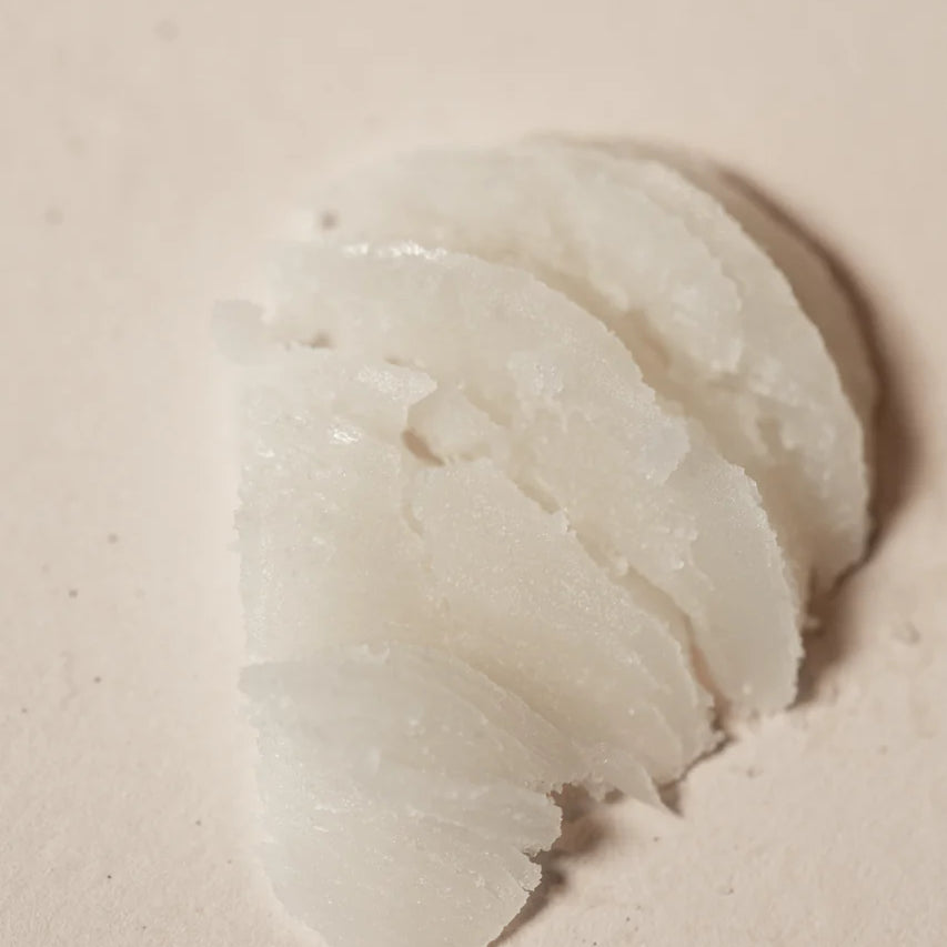 A close-up of several thin, uneven slices of Oway Precious Wax by Oway, a white, luminous, shine-enhancing styling wax for natural definition, displayed on a beige surface.