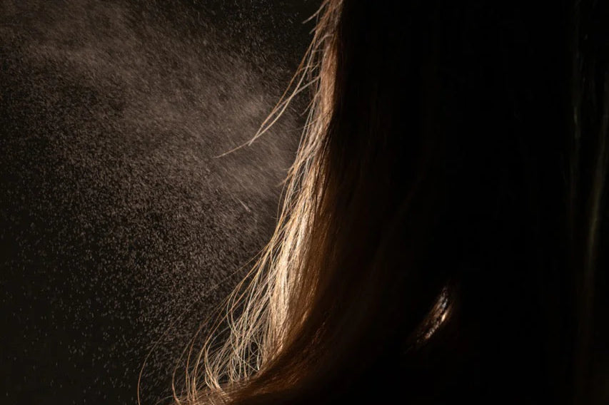 Oway Phytoprotein Mist, a leave-in treatment, is sprayed on the back of fragile, stressed hair, with visible droplets highlighted against a dark backdrop to showcase its plant-based protein strength.