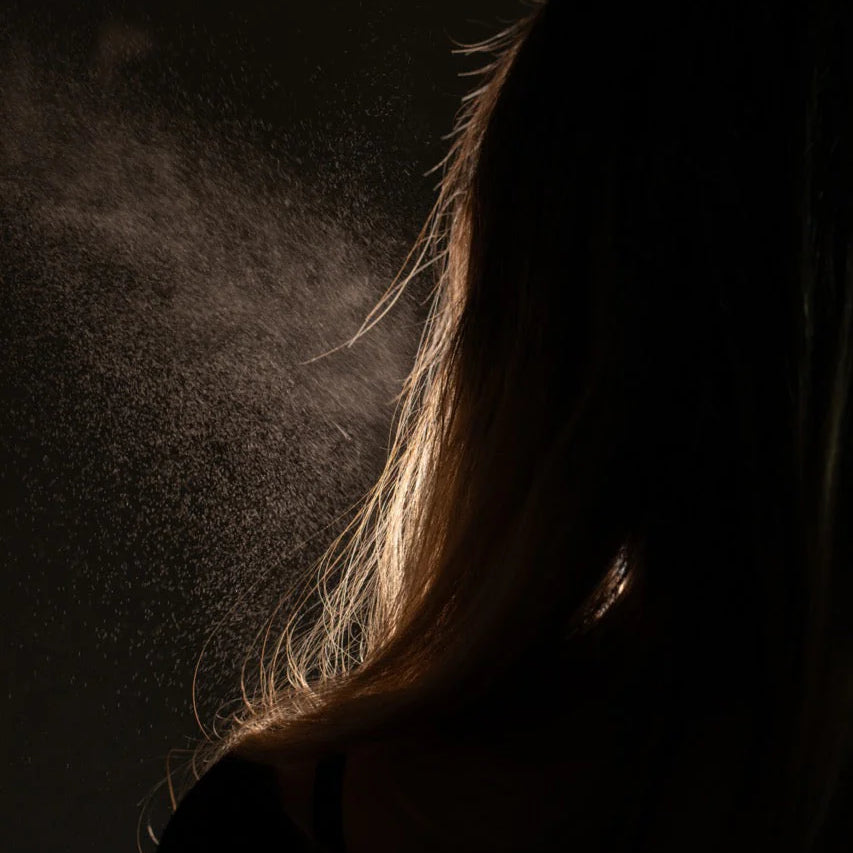 Oway Phytoprotein Mist, a leave-in treatment, is sprayed on the back of fragile, stressed hair, with visible droplets highlighted against a dark backdrop to showcase its plant-based protein strength.