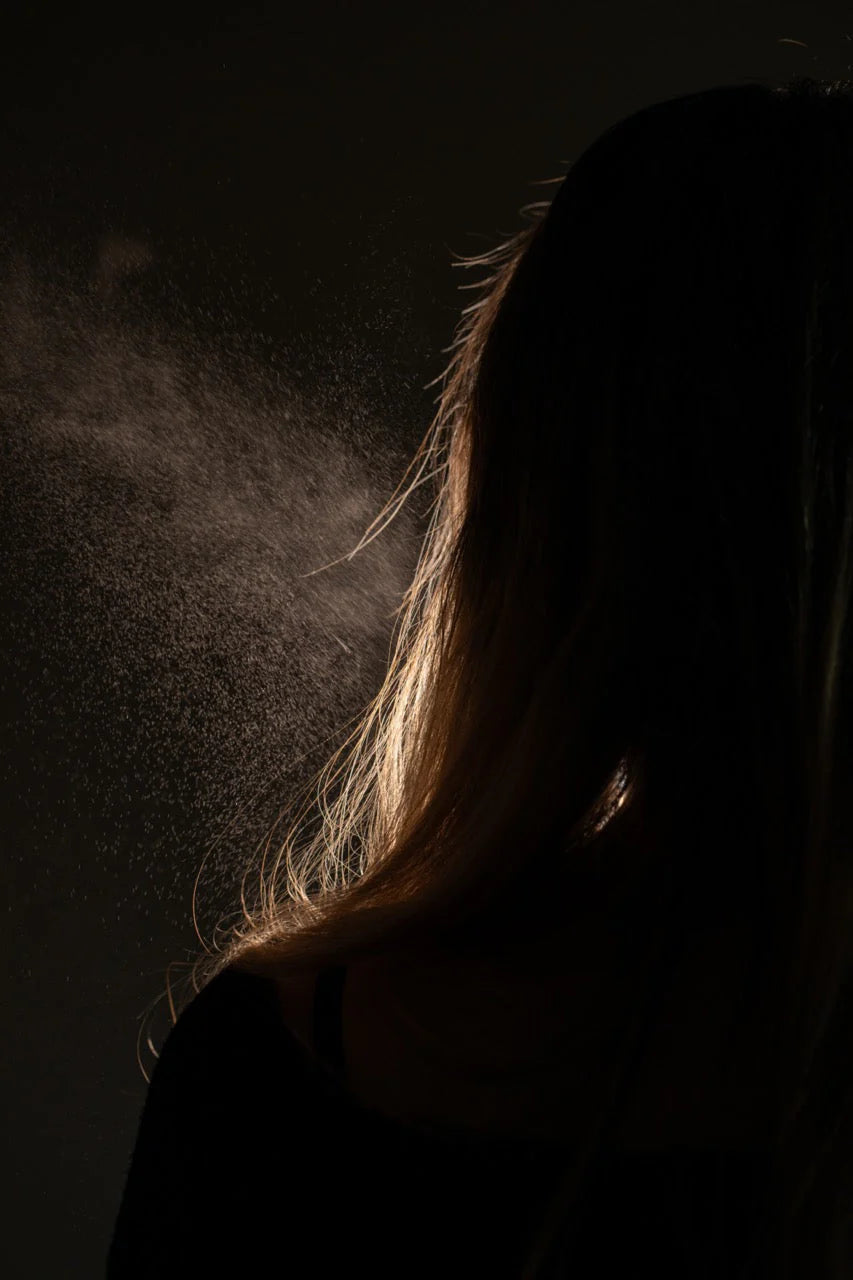Oway Phytoprotein Mist, a leave-in treatment, is sprayed on the back of fragile, stressed hair, with visible droplets highlighted against a dark backdrop to showcase its plant-based protein strength.