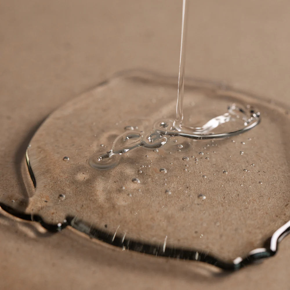 Oway Purifying Hair Bath for Oily Scalp from Oway is poured onto a flat, beige surface, forming a bubble-filled pool—perfect for oily scalps and gentle dandruff care.
