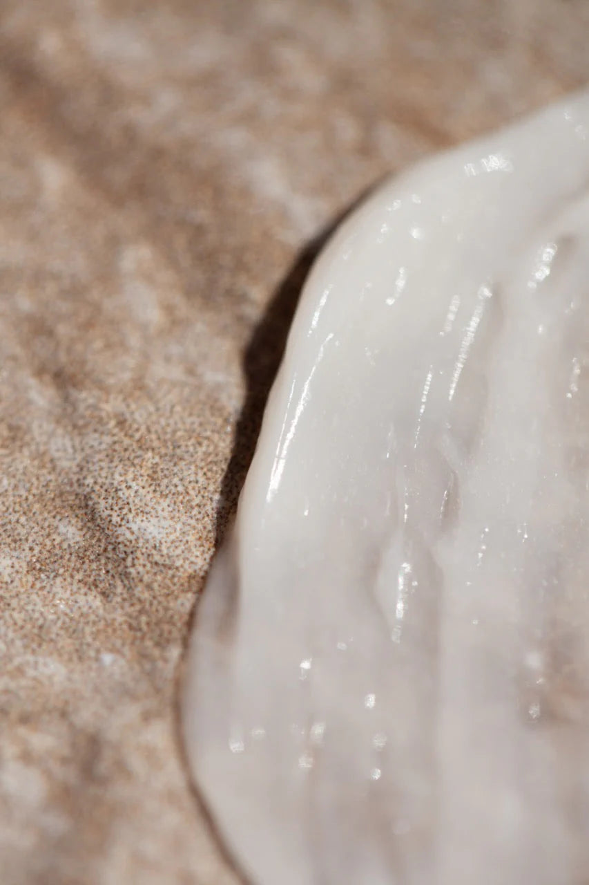 Close-up of Oway Rebuilding Hair Mask, a white creamy restorative mask by Oway, spread on a textured brown surface—ideal for instant repair and nourishment of damaged or chemically treated hair.