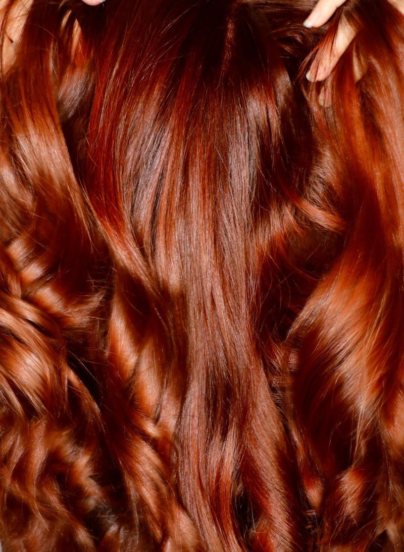 Close-up of wavy red hair with a hand gently holding it.