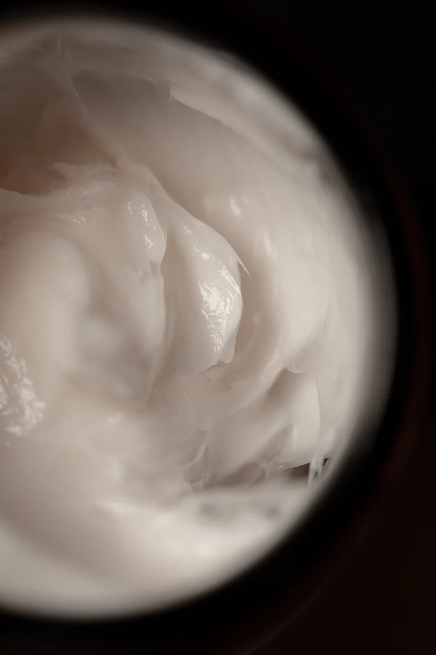 A close-up of Oway Shaping Putty, a creamy white styling putty by Oway, provides medium hold and a natural finish for sculpted texture inside its container.
