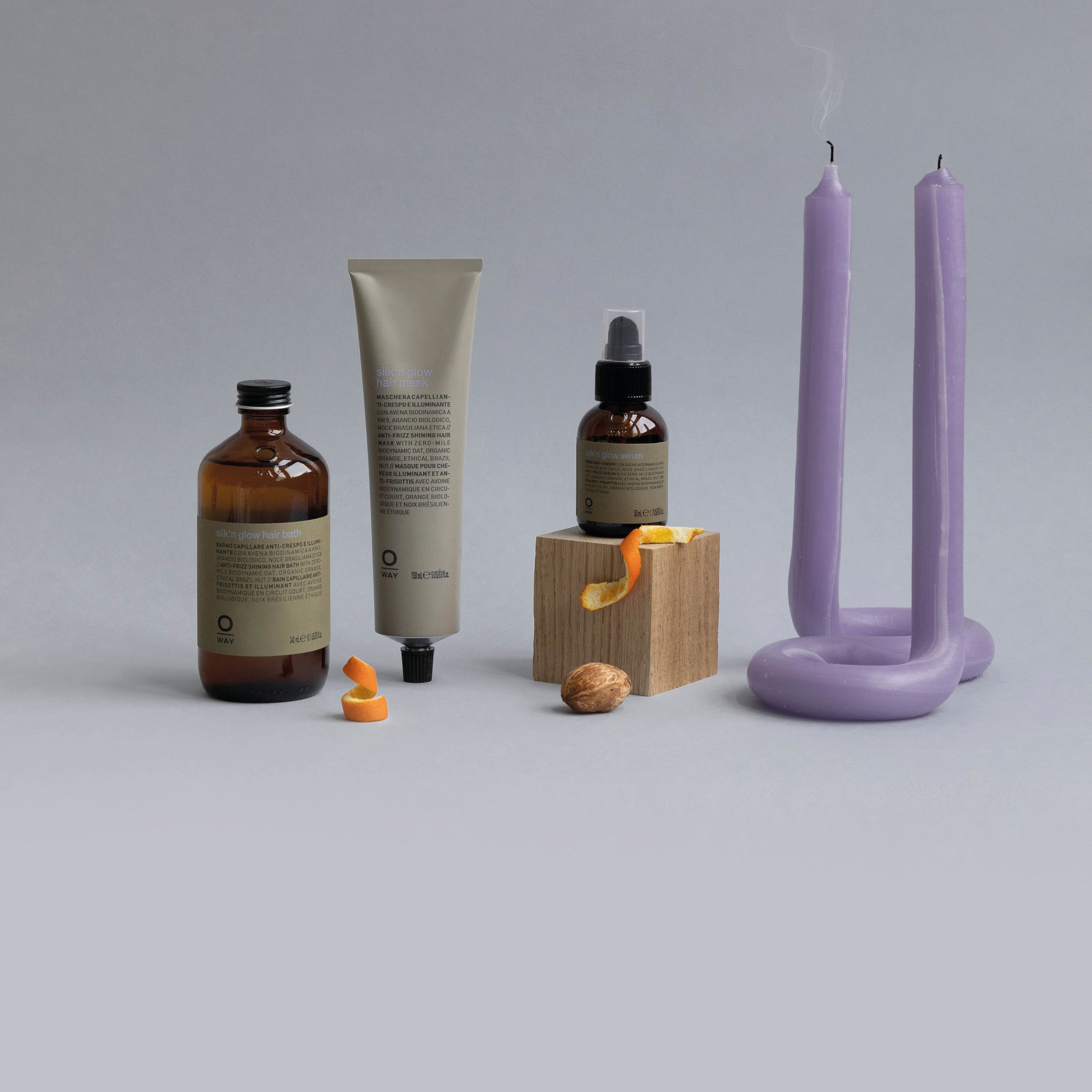 Three skincare items, a wooden block with orange peel, a walnut, and a lavender U-shaped candle sit on a gray surface—perfect inspiration for Oway Silk’N Glow Hair Bath, a taming hair bath for frizz-prone hair by Oway.
